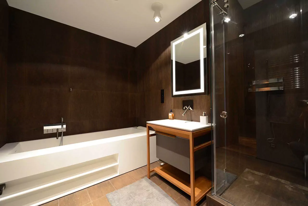 A custom-lighted mirror is above a single sink with a white bathtub in the shower room.