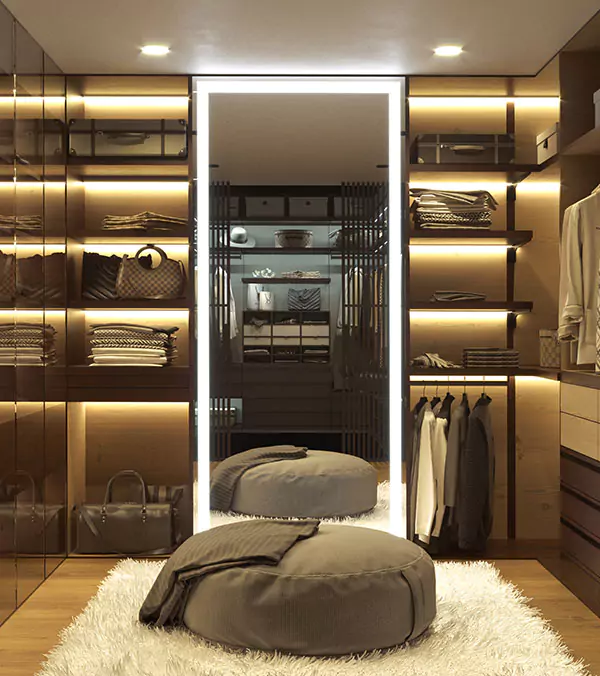 A snippet of a walk-in dressing area with a modern lighted mirror and round floor cushion.