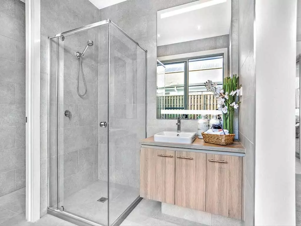 A lighted mirror and an elegant single sink above a wooden cabinet in a shower room.