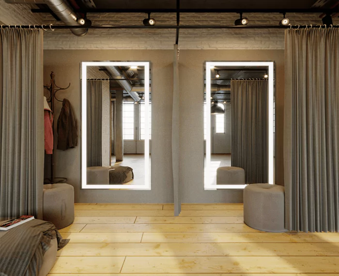 Two full-length lighted mirrors in a fitting room with a brown round foam stool.